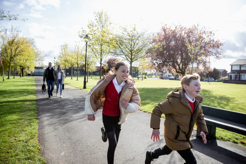 Young boy and girl in school uniform running, with a man and woman in the background